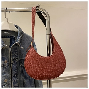 Detail shot of a red-brown crescent underarm bag with crocodile pattern hanging on a rack