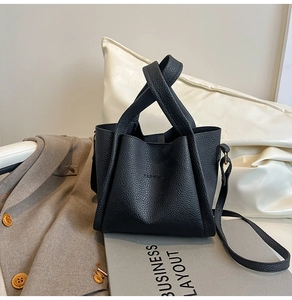 Detail of black lychee grain leather texture and embossed FASHION text on bucket bag