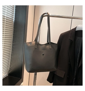 Detail view of black leather tote bag with large front pocket and elegant round button