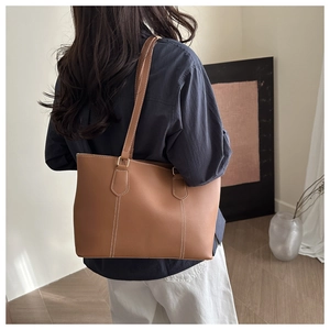 Detail of a brown leather tote bag with white contrast stitching on model back