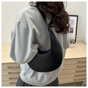 Rear view of a minimalist black crescent shoulder bag styled on a female model