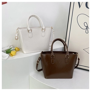 Detailed view of minimalist white and dark brown leather bucket bags on a white podium