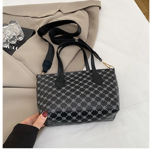 Detail of black monogram tote bag with white floral pattern and wide fabric shoulder strap
