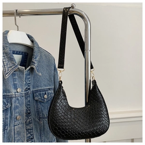 Detalle de la textura de cuero trenzado negro y hebilla metálica del bolso hobo