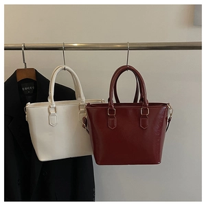 Detail view of large minimalist leather tote bags in white and dark red hanging on a rack