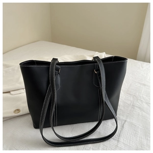 Close-up of black tote bag featuring white contrast stitching and fine leather texture