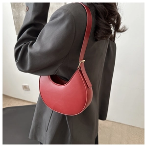 Detail of red crescent shoulder bag with matte leather texture and gold buckle on model