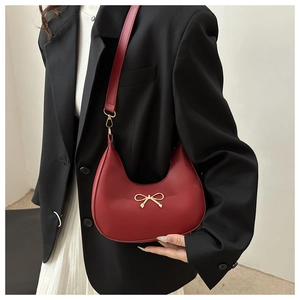 Detail of red crescent shoulder bag with golden bow ornament and leather strap