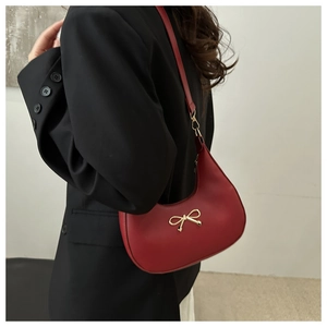 Side view of red matte leather crescent bag with gold bow ornament and slim shoulder strap