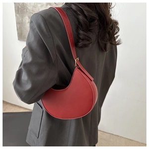 Close-up of a red crescent shoulder bag on a model showing size and fit with dark grey blazer