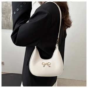 Close-up of creamy white half-moon bag featuring a gold metal bow and smooth texture