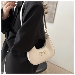 Close-up of a cream crescent hobo bag featuring a golden bow buckle and leather strap