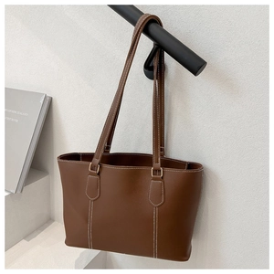 Detail of brown leather tote bag with white contrast stitching and slender shoulder straps