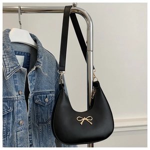 Detail of a black crescent hobo bag featuring a gold bow accent and wide strap
