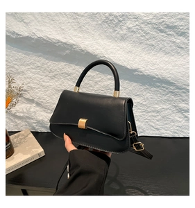 Dettaglio della texture in pelle nera opaca e della fibbia dorata di questa piccola borsa quadrata