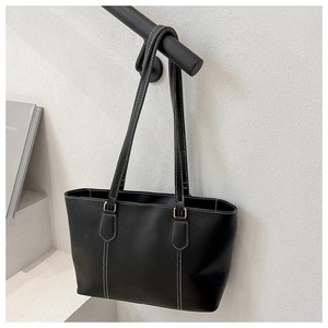 Close-up of black tote bag featuring fine white contrast stitching and gold metal buckles