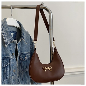Detail of dark brown crescent hobo bag with a decorative gold bow buckle on denim jacket