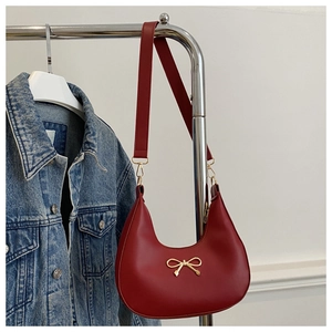 Detail of red crescent hobo bag with golden bow hardware and leather shoulder strap