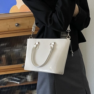 Glossy white patent leather bucket bag with top handles and adjustable shoulder strap