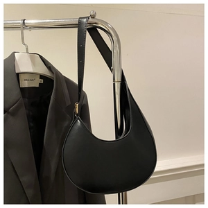 Close-up of black crescent shoulder bag with adjustable strap on a minimalist display
