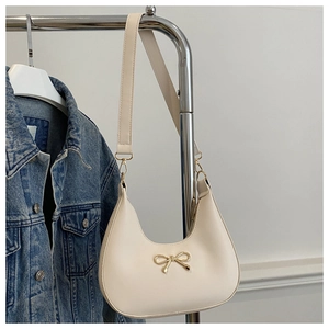 Detail of a creamy white crescent bag with golden bow hardware and soft leather texture
