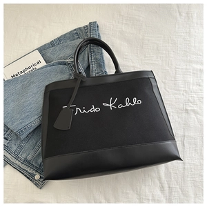 Detail of black canvas tote bag featuring Frida Kahlo signature and leather trim