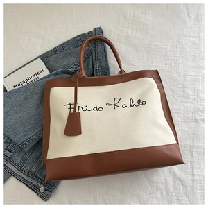 Detail of canvas tote bag with brown leather handles and Frido Kahlo text print