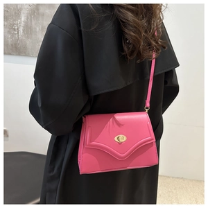 Borsa a tracolla rosa acceso con chiusura a scatto dorata su sfondo cappotto nero