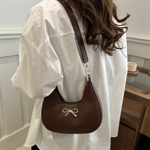 Chic brown crescent shoulder bag with a gold bow accent, stylish French vintage aesthetic