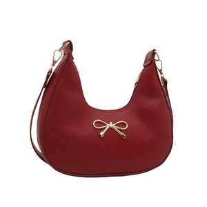 Red crescent shoulder bag with golden bow hardware and adjustable strap on white background