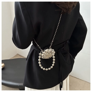 Detail of silver shell-shaped mini bag with pearl handle and metal chain on a black blazer