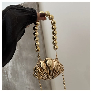 Detail of a golden shell-shaped clutch bag with beaded handle and metallic chain strap
