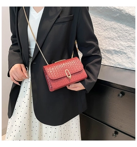 Detail of a dark red woven crossbody bag with gold chain strap worn by a female model