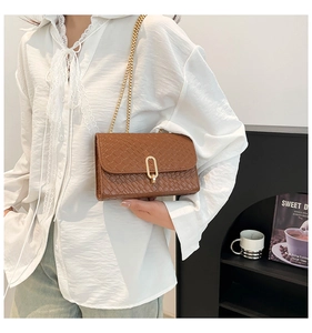 Close-up of brown woven texture crossbody bag featuring a golden oval metal lock and chain
