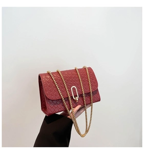Detail of burgundy woven leather texture and golden metal oval clasp on a small flap bag