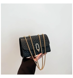 Detail of black woven texture on flap bag with gold chain strap and metal clasp