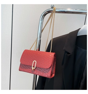 Detail of red snake-patterned leather crossbody bag with elegant gold oval lock and chain