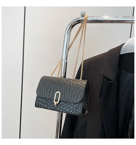 Close-up of black woven leather texture and elegant gold oval metal clasp on flap bag