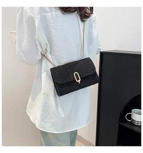 Detail view of black crossbody bag with gold metal chain strap on model in indoor setting