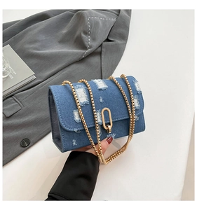 Detail of distressed denim crossbody bag with gold oval lock and metal chain strap