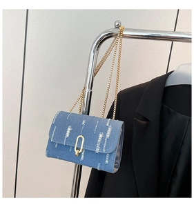 Detail of denim crossbody bag with distressed fringe stripes and gold chain strap