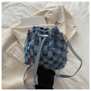Detail of blue denim checkerboard bucket bag with frayed fringe and gold hardware