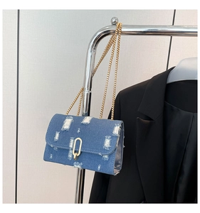 Detail of blue denim crossbody bag with frayed edges and golden metal chain strap