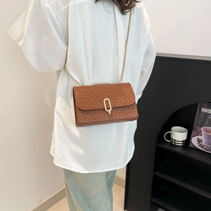Chic brown woven shoulder bag with gold chain strap worn by a model in a casual outfit