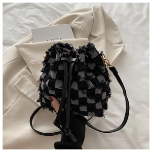 Detail of checkered drawstring bucket bag featuring frayed edges and gold metal hardware