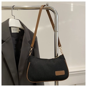 Detail of black twill hobo bag with brown leather trim and golden zipper on a metal stand