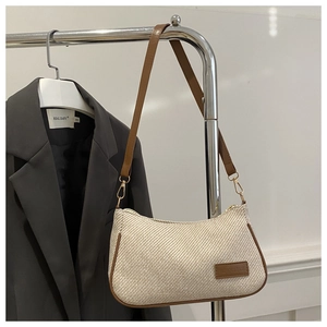 Detail of beige woven hobo bag with brown leather trim and metallic fashion label
