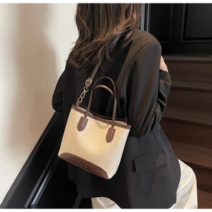 Chic beige canvas tote bag with brown leather trim worn as a stylish shoulder bag