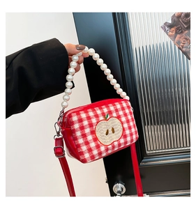 Detail of red checkered bag featuring apple embroidery and elegant white pearl handle