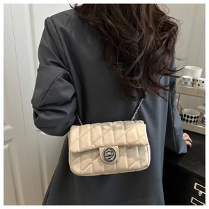 Close-up of beige quilted crossbody bag with metal chain strap worn by a model